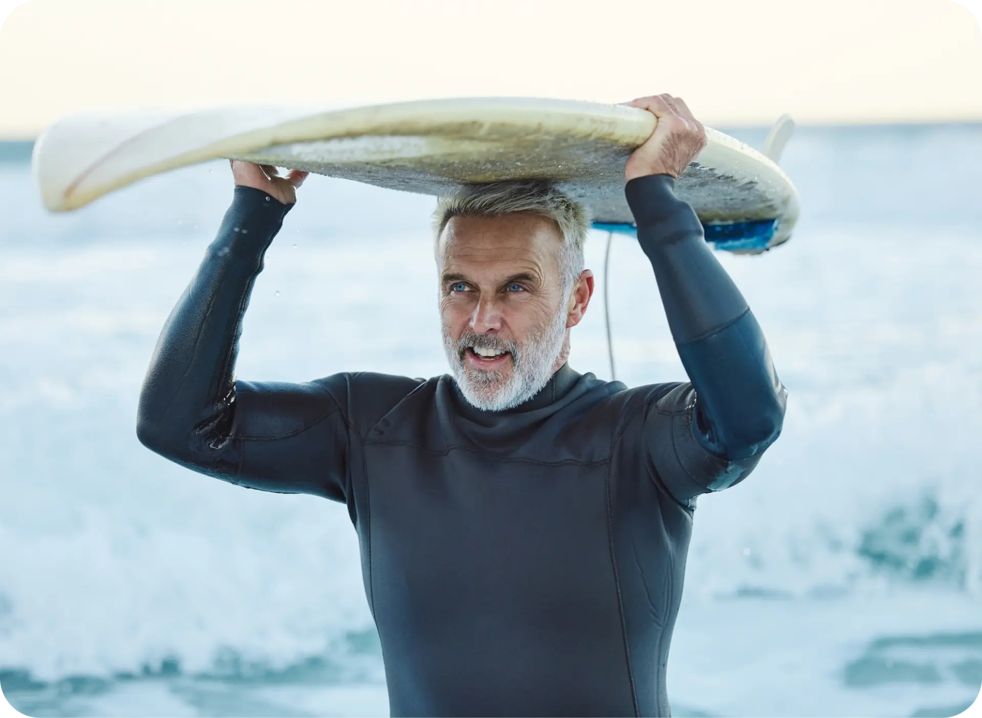 Active older adult carrying a surfboard at the beach